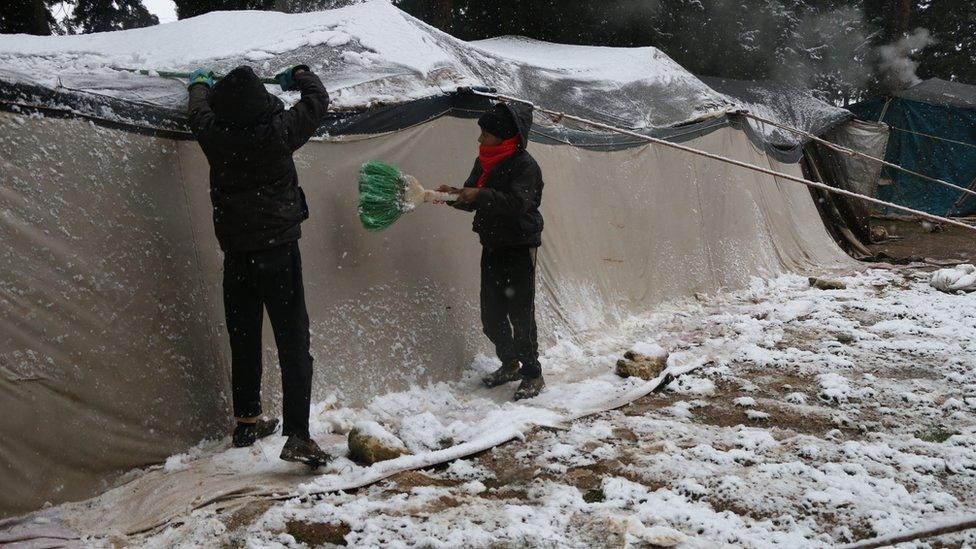 Children clear snow off the roof of a tent a camp for displaced people in Aleppo province, Syria