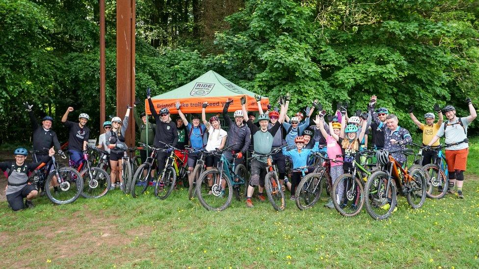 A group of cyclists in Ashton Court in Bristol smile and wave at the camera