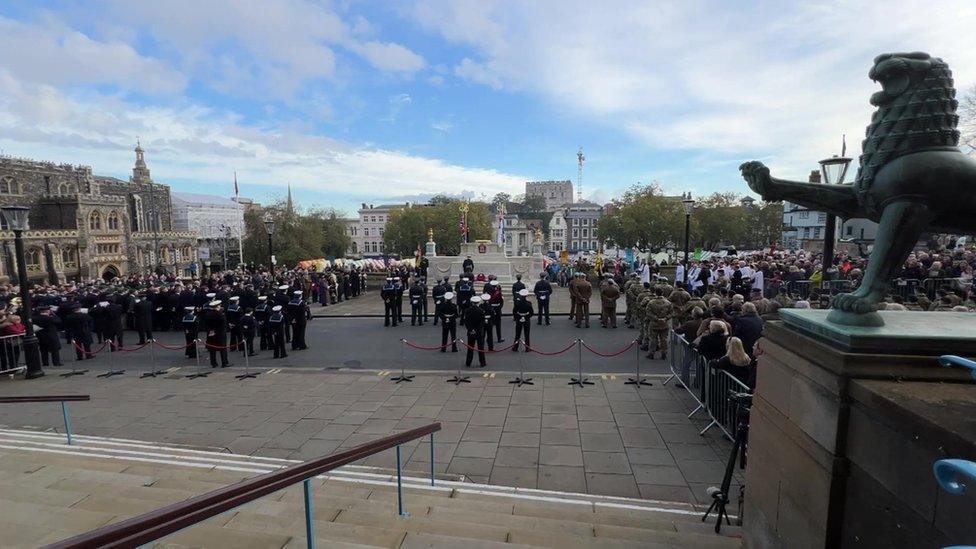 Wide shot from the steps of Norwich City Hall, showing the lion statue on the left and the parade assembled around the war memorial in the background