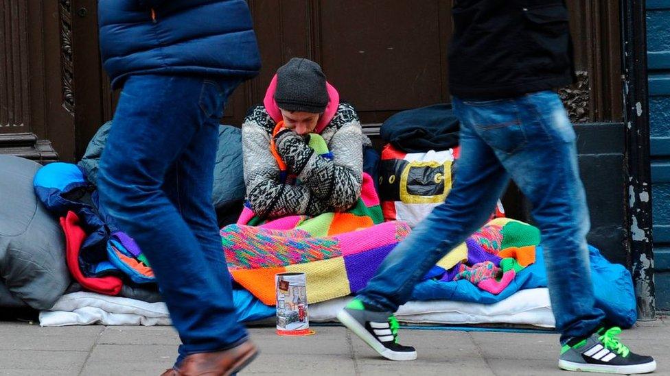 Woman in roadside bed with people walking past