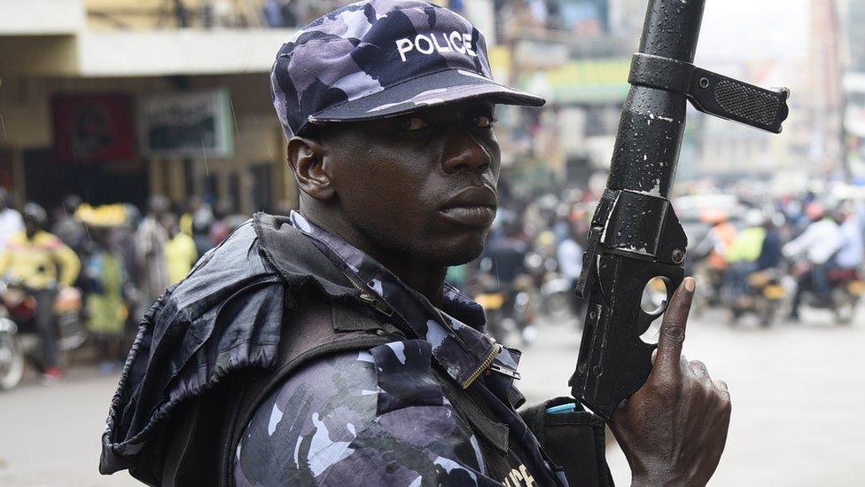 A police officer is seen lifting a teargas launcher opposite protesters during a demonstration on July 11, 2018 in Kampala to protest a controversial tax on the use of social media