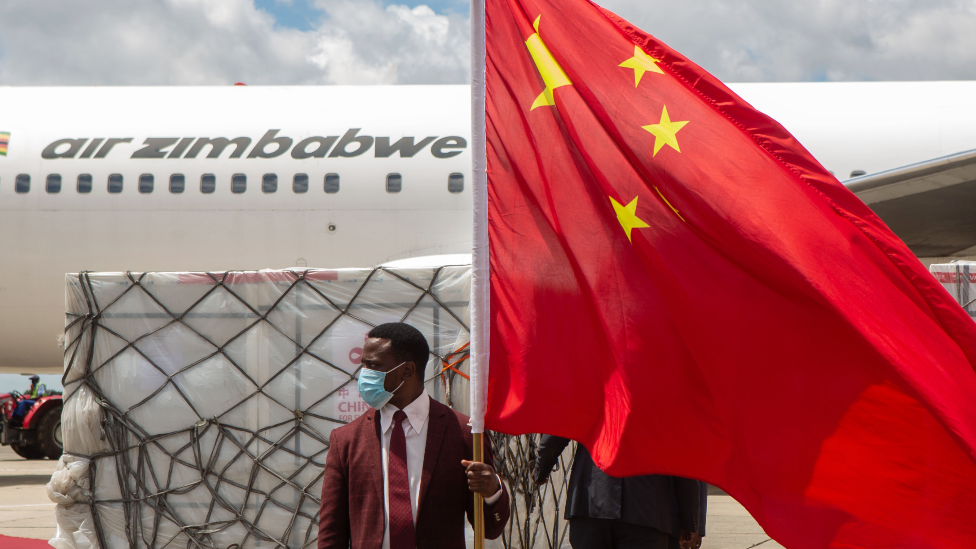 A man holds a Chinese flag in front of the shipment of Sinovac and Sinopharm vaccines at Harare International Airport, Zimbabwe - March 2021