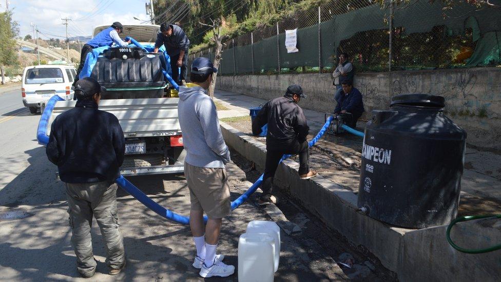People in La Paz stand next to a lorry delivering water