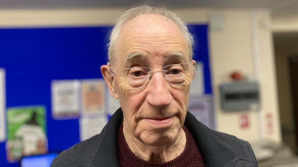 Man with very short grey hair stands in a library