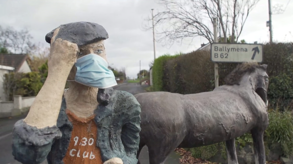 A sculpture of a farmer wearing a surgical mask next to a sculpture of a horse in Cullybackey