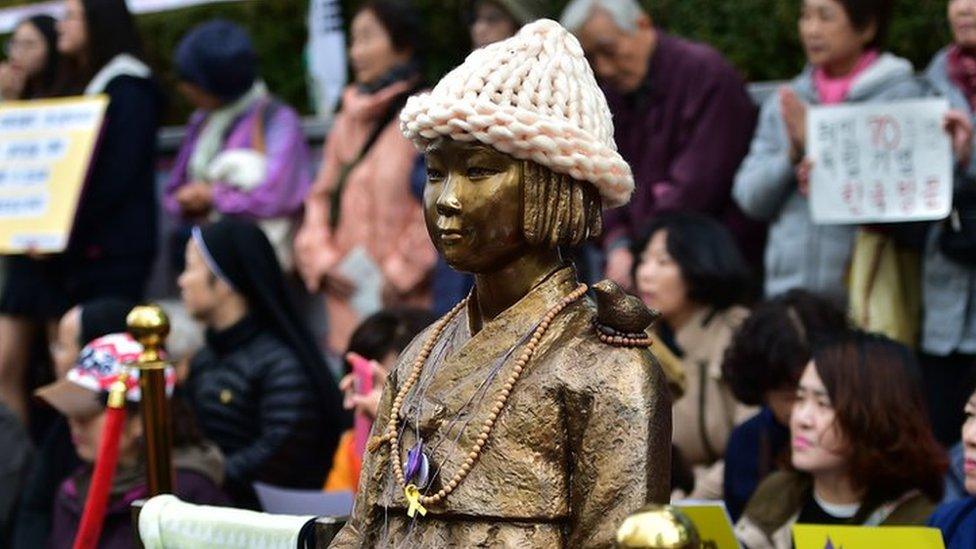 Protestors sit next to a statue (C) of a South Korean teenage girl in traditional costume called the 'peace monument' for former 'comfort women' who served as sex slaves for Japanese soldiers during World War Two, during a weekly anti-Japanese demonstration near the Japanese embassy in Seoul on 11 November 2015.