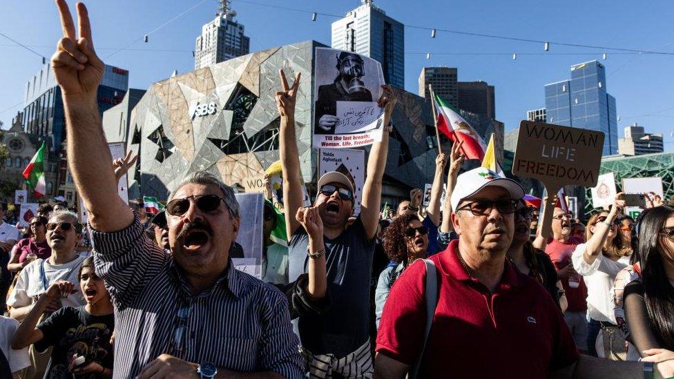 Three men hold placards and banners and display peace signs during a rally in Melbourne, Australia