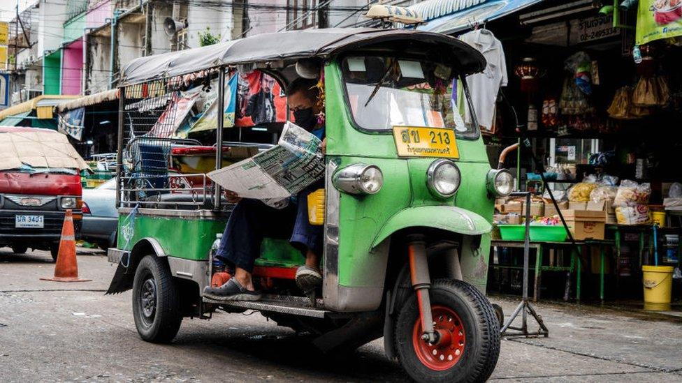 A Tuk Tuk driver reads a newspaper while waiting for customers in Bangkok