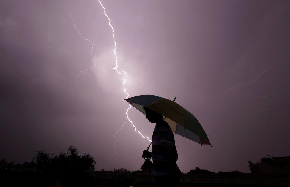 A pedestrian walks with an umbrella as lightning strikes during an evening thunderstorm in Jammu on May 14, 2015.