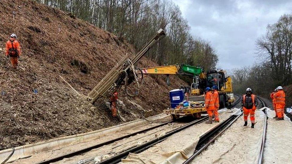 Image shows workers and equipment on a bank alongside a railway line