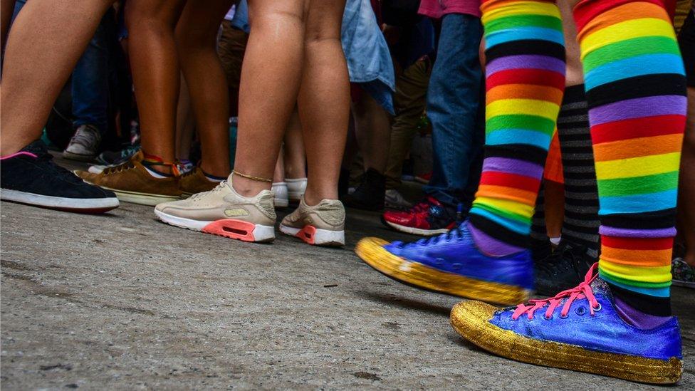 A group of people with only their legs showing, including one person with rainbow-coloured socks