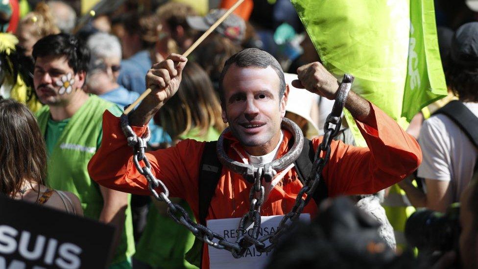 A protester wearing a prison outfit with a mask of President Macron