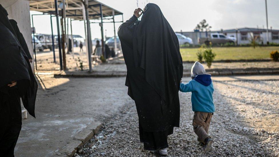 A woman walks with her child at a camp in north-eastern Syria