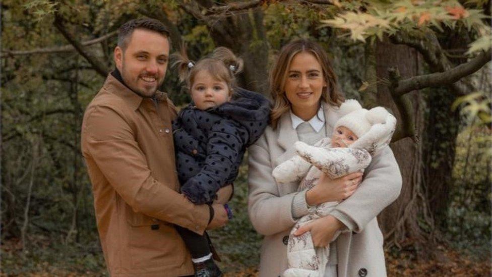 A dad and mum holding two children in the woods