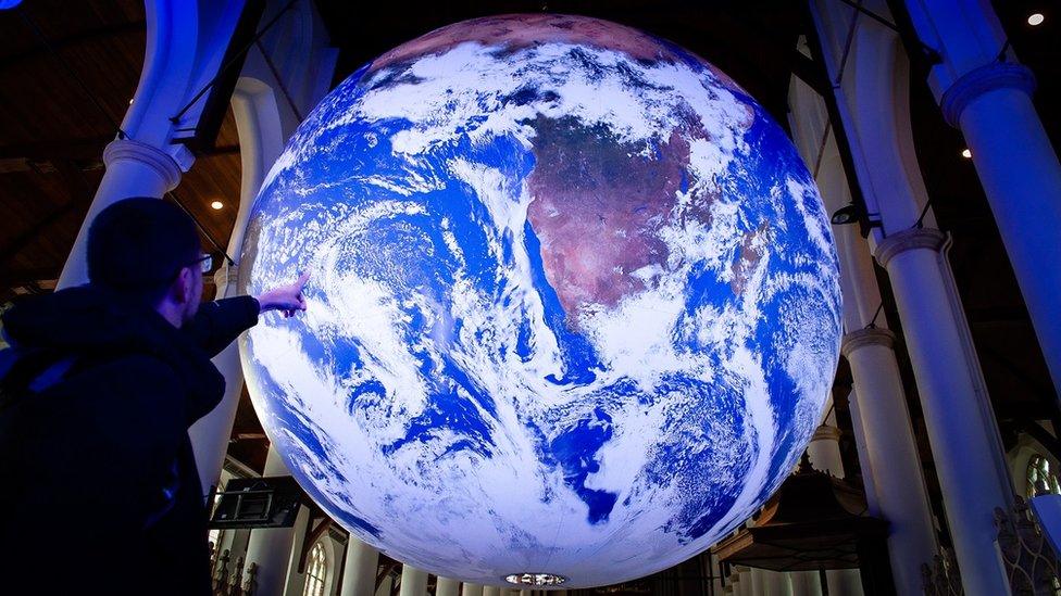 A man points at the giant Earth created by artist Luke Jerram