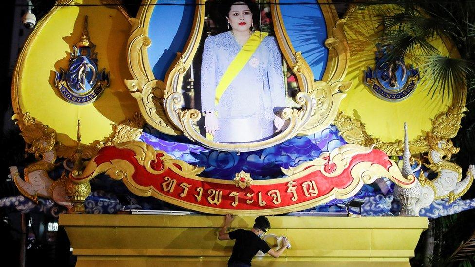 A person spray-paints a pedestal, above which stands a depiction of Queen Mother Sirikit