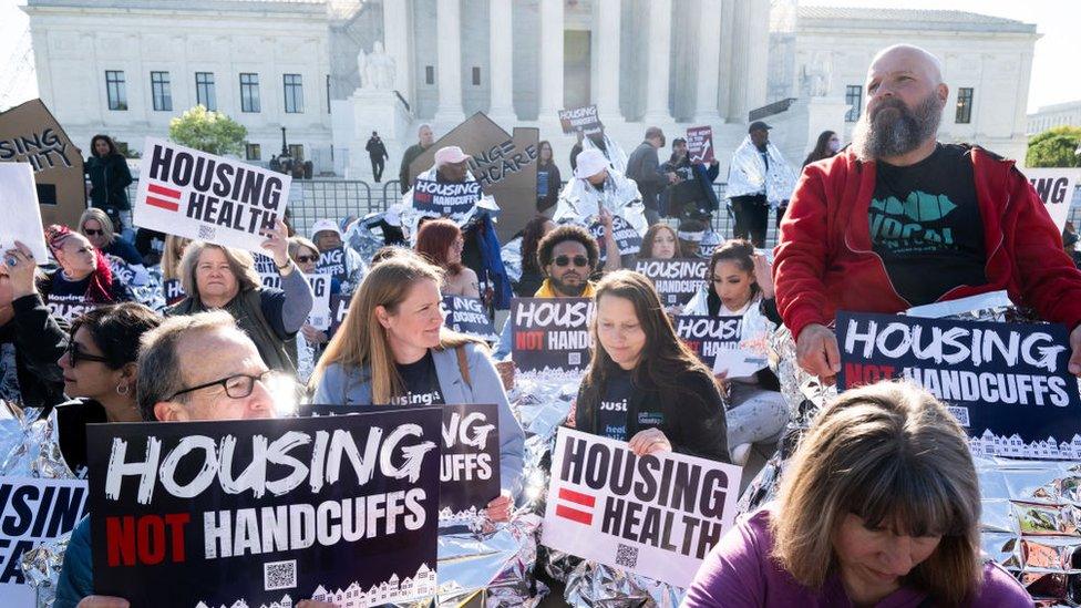 Demonstrators hold signs and use reflective blankets during a protest outside the US Supreme Court in Washington, DC, April 22, 2024 by homeless activists as the Court hears the case of City of Grants Pass v. Johnson that could make it illegal to sleep outside