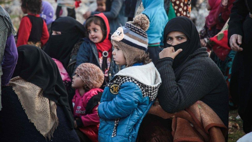 Displaced Syrians from Idlib province queue to receive food aid from a truck