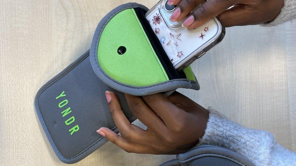 A person removing a phone from a lockable pouch