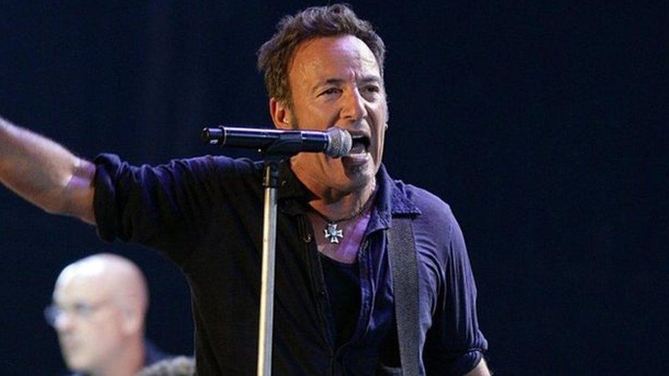 Bruce Springsteen sings into a microphone while holding a guitar