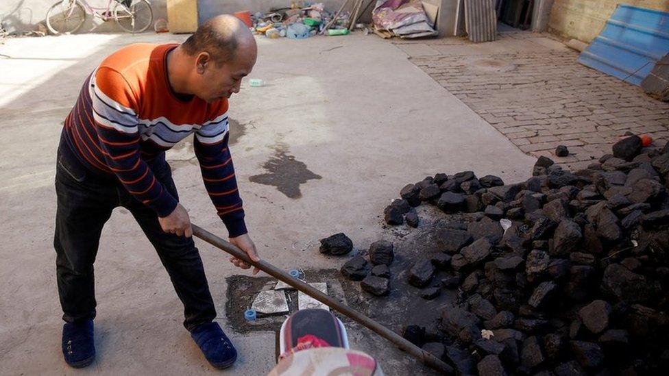 A man shovels coal he uses to heat his home in his courtyard in the village of Heqiaoxiang outside of Baoding, Hebei province, China, December 5, 2017