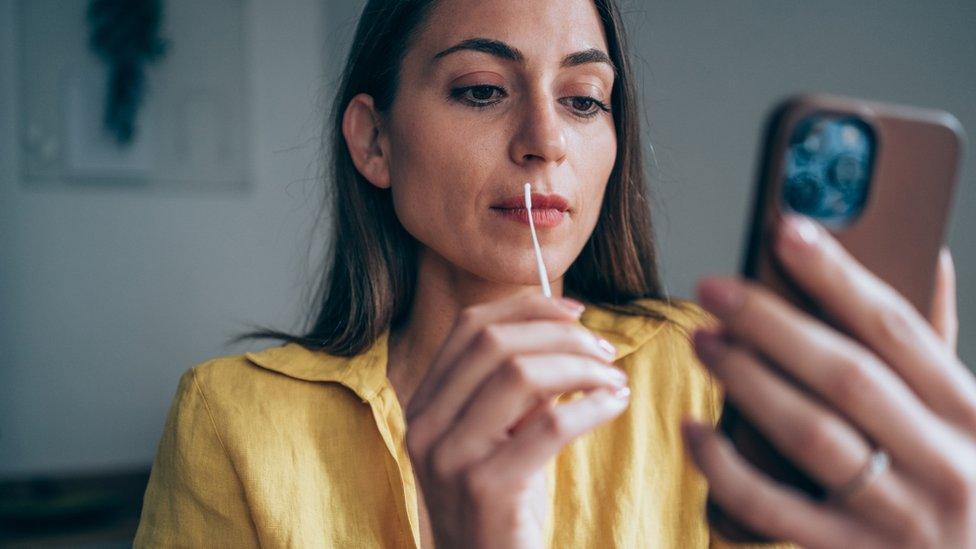 A woman swabs her throat while looking at her phone screen