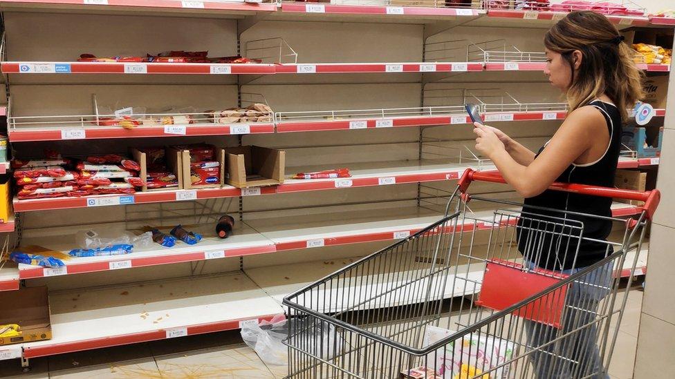 A woman takes a picture of noodles on the floor in front of empty pasta shelves at a supermarket, as people began stockpiling food following the coronavirus outbreak, in Buenos Aires