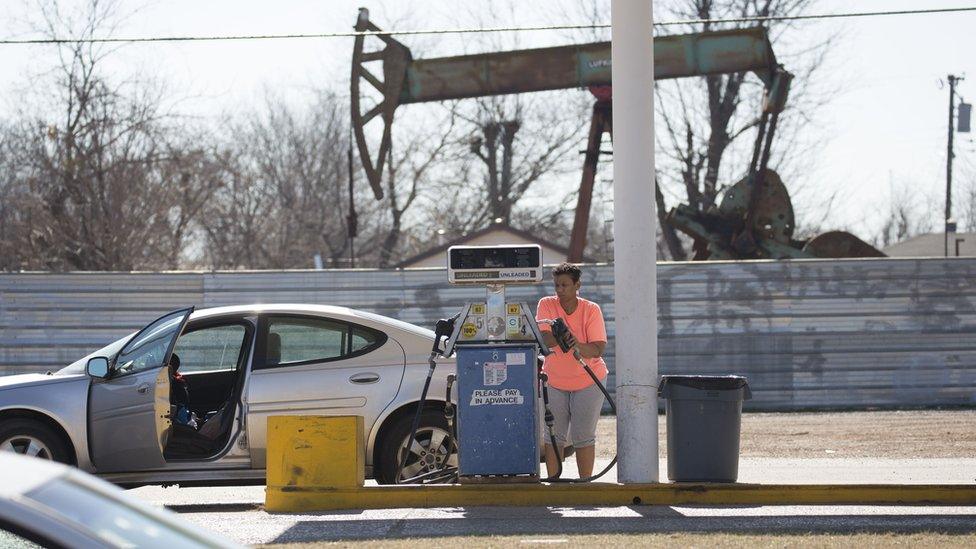 Women pumping gas with oil rig in background