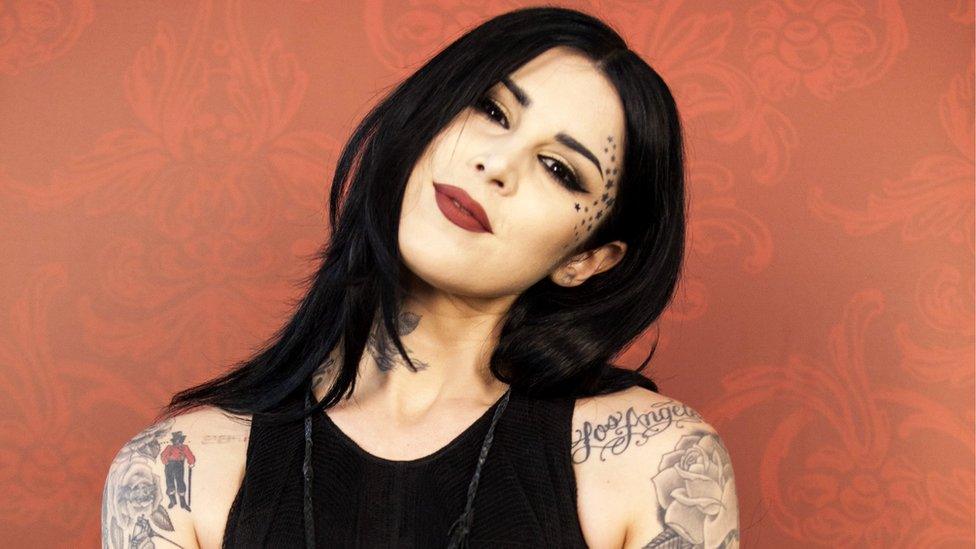 Kat Von D posing at press event on red flock background