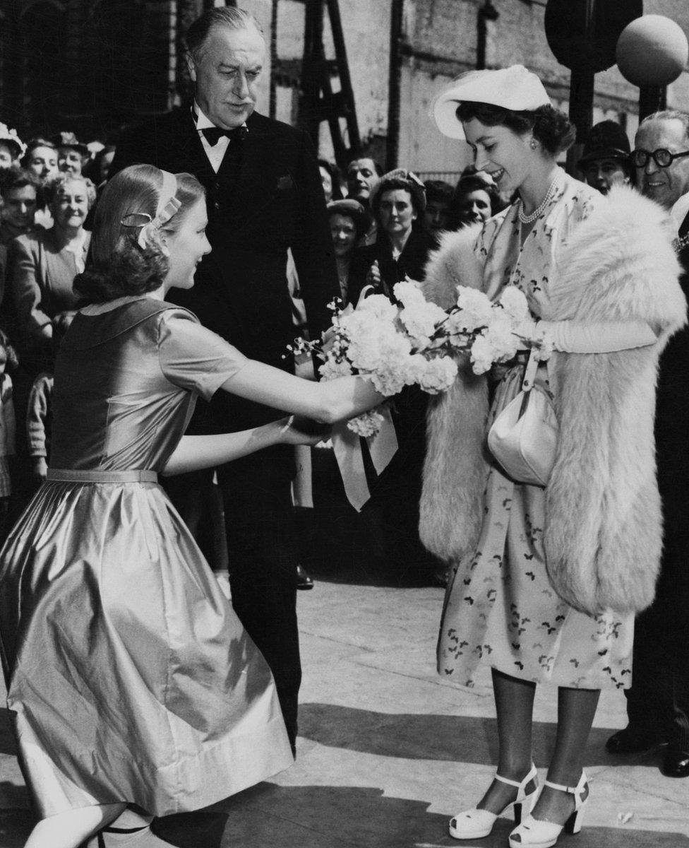 Princess Elizabeth accepts a bouquet offered by Anna Massey, daughter of actor Raymond Massey, outside a London theater in 1951