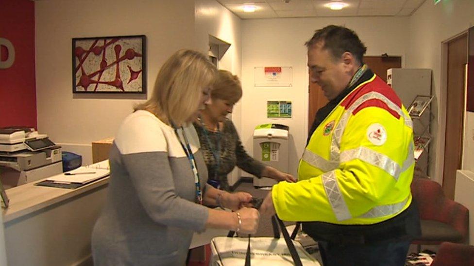 A blood biker hands over a milk delivery