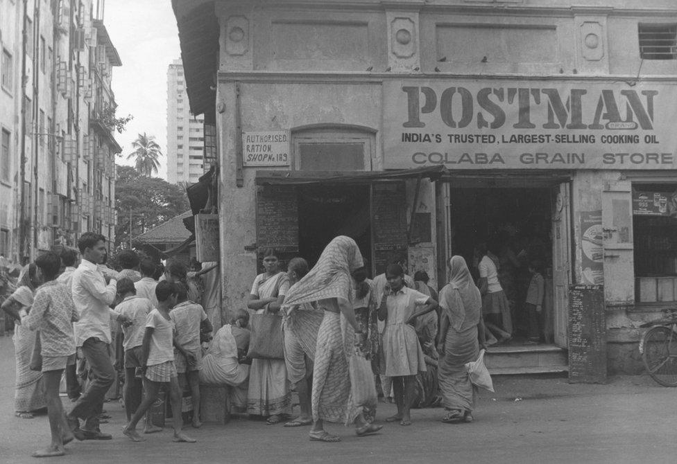 circa 1970: Customers queue outside a dry food shop in Bombay, India.