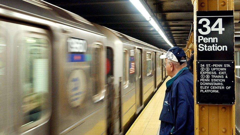 A commuter waits at New York City's Penn Station as a subway train approaches.