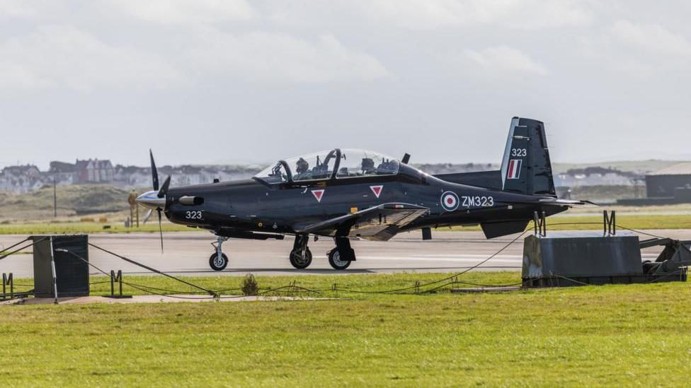 A Beechcraft Texan T1 aircraft seen taxiing to runway to provide basic flying training at RAF Valley. The plane has two seats one in front of the other and is black