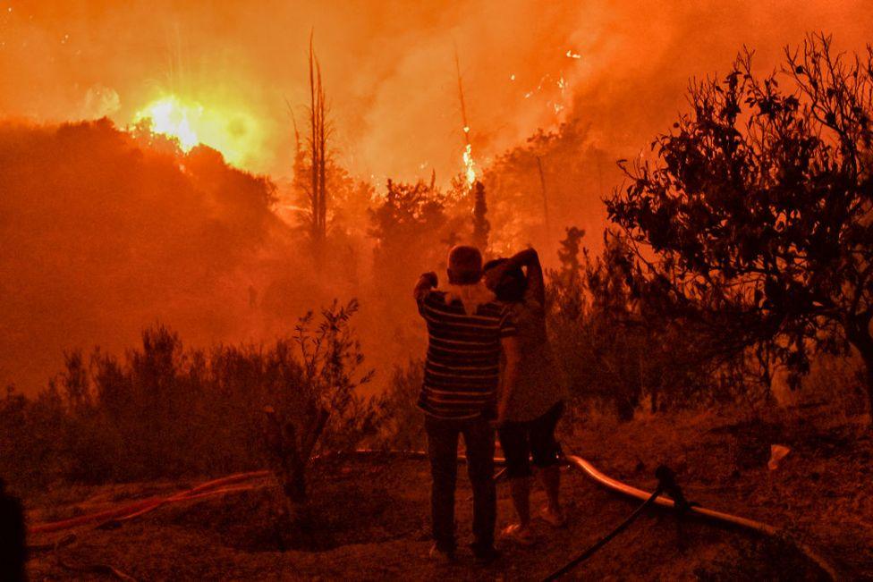 A couple look on at a wildfire raging in the village of Ano Loutro, south of Athens, on 30 September, 2024.