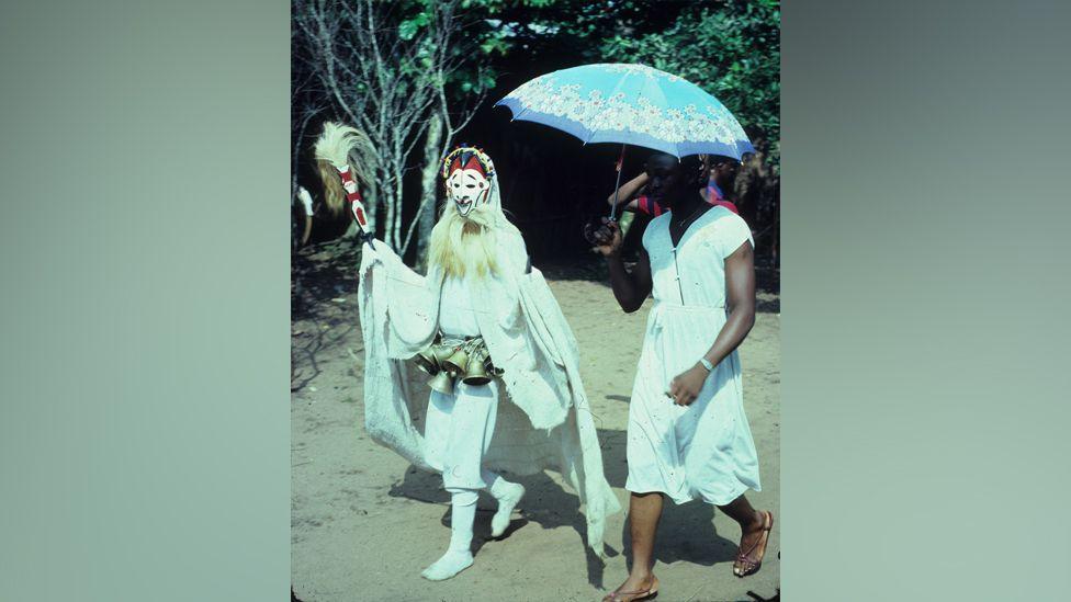 A person with a mask on walking next to someone holding a parasol