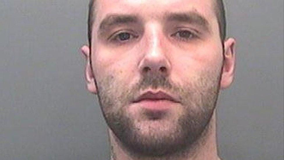 A custody image of David Braddon. He has dark stubble and looks at the camera with a neutral expression. 