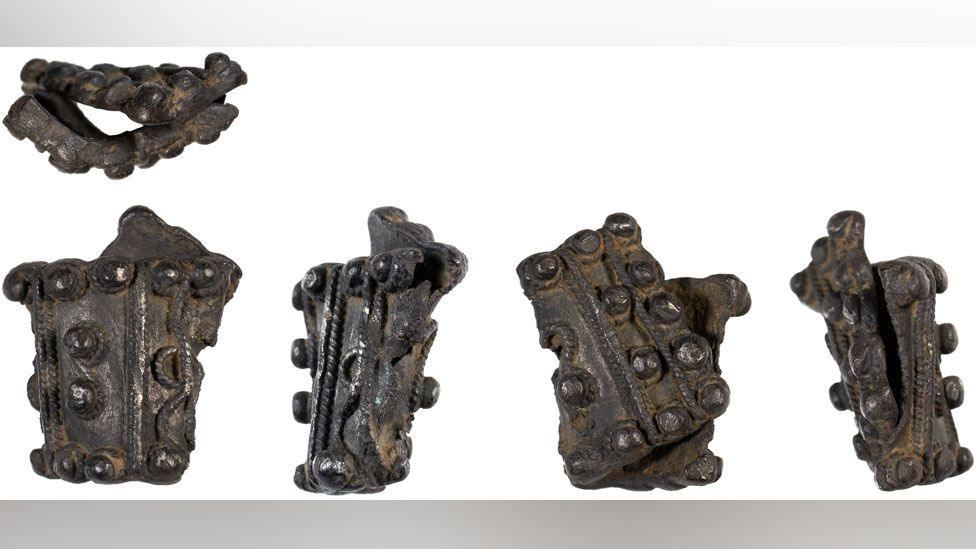 Five views of an early medieval silver brooch. It is folded in half. There are four views along the bottom and one view of it on its side top left. The brooch is divided by strands of corded wire. It has raised solid bosses running along its width.