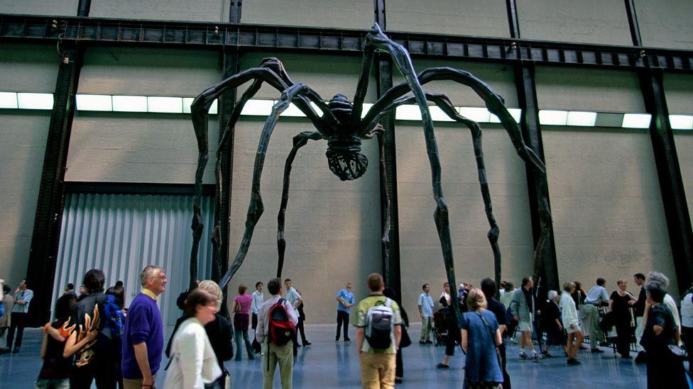 A giant metal black spider with long spindly legs towering over several dozen visitors inside Tate Modern's Turbine Hall in 2000