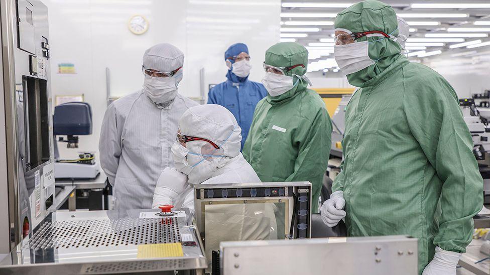 Defence Secretary John Healey and Newton Aycliffe and Spennymoor MP Alan Strickland being shown kit in the semiconductor facility clean rooms. Everyone is wearing full-body hazmat-style overalls and face coverings. The visitors' are green, while others are wearing white or blue.