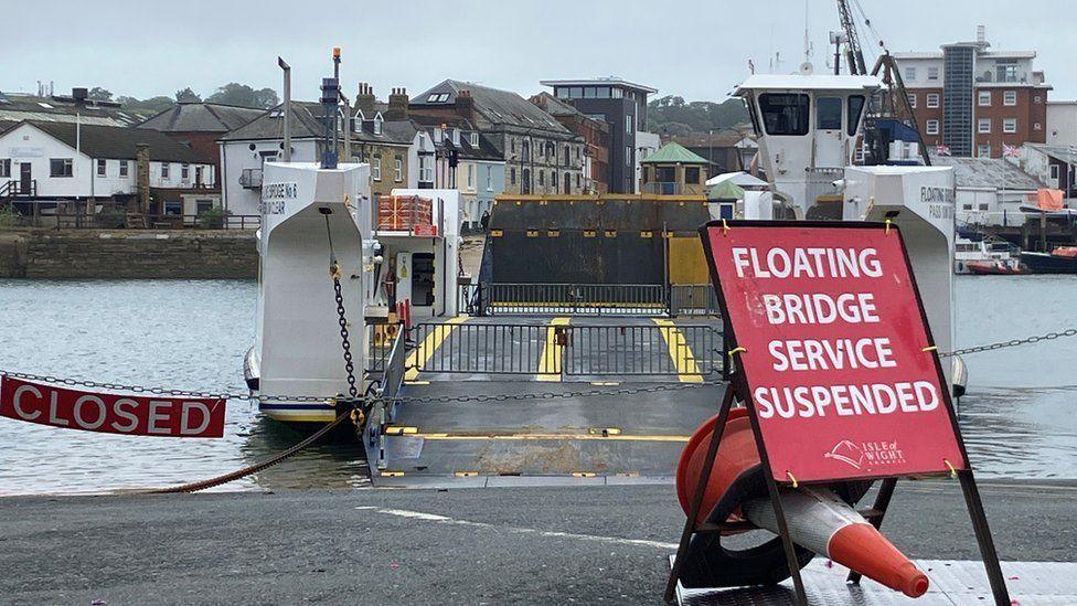 Chain across slipway with ferry stopped and gates closed in the water - buildings can be seen across the water.