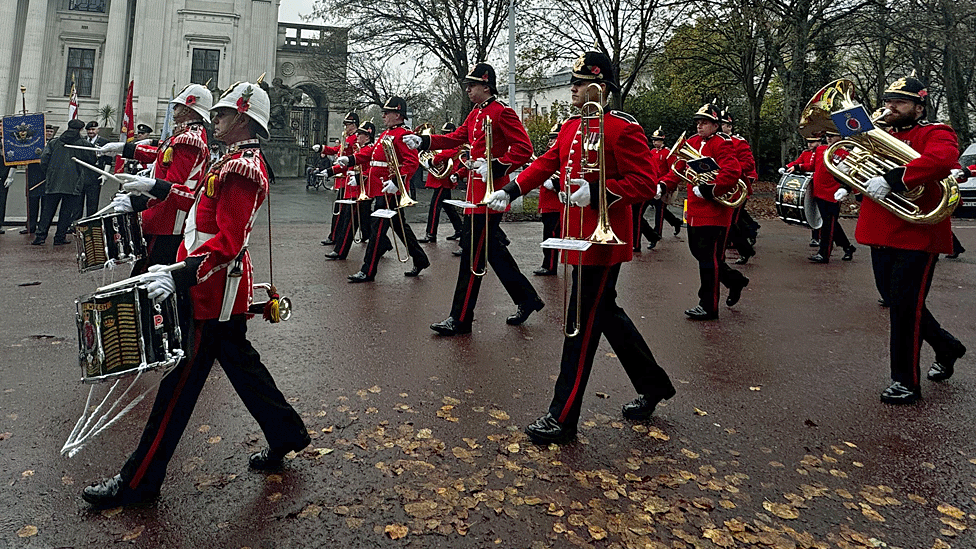 Military band with drums and brass instruments march past City Hall in Cardiff