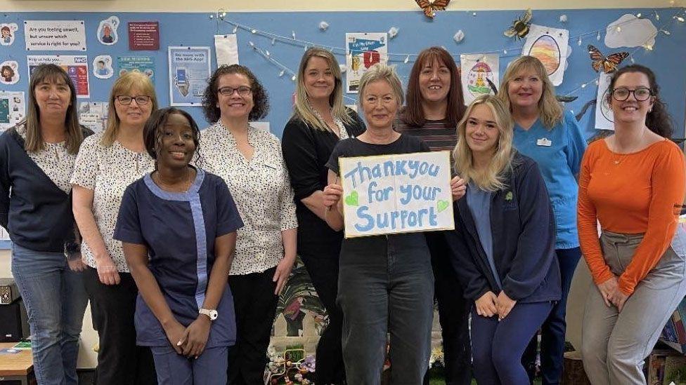 Dr Ann Robinson standing with her staff holing a sign that says thank you for your support