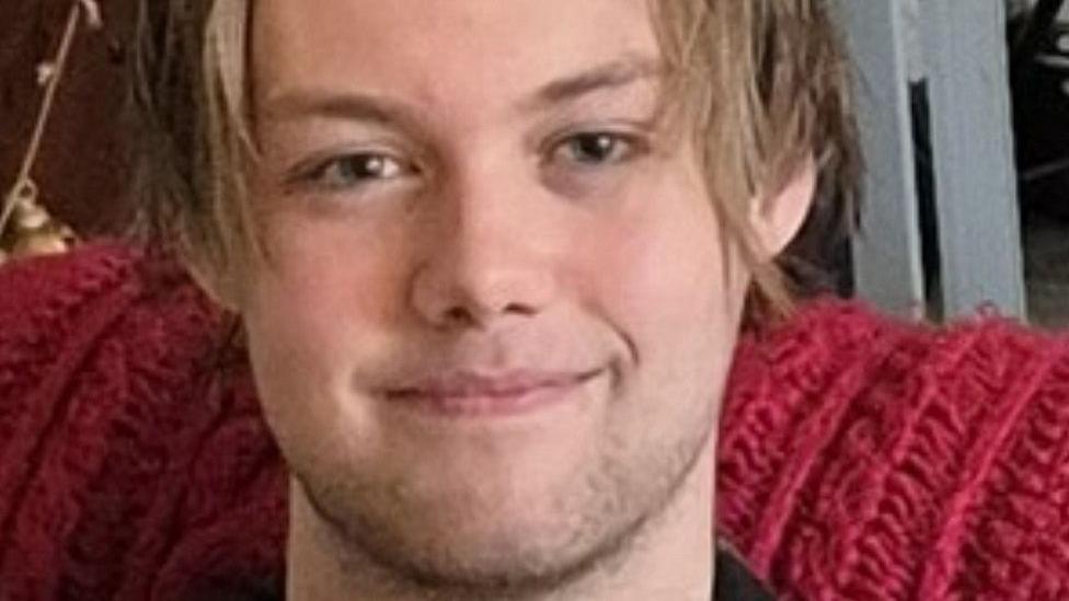 Ashton Kitchen-White smiling at the camera with a stubble beard and brown 