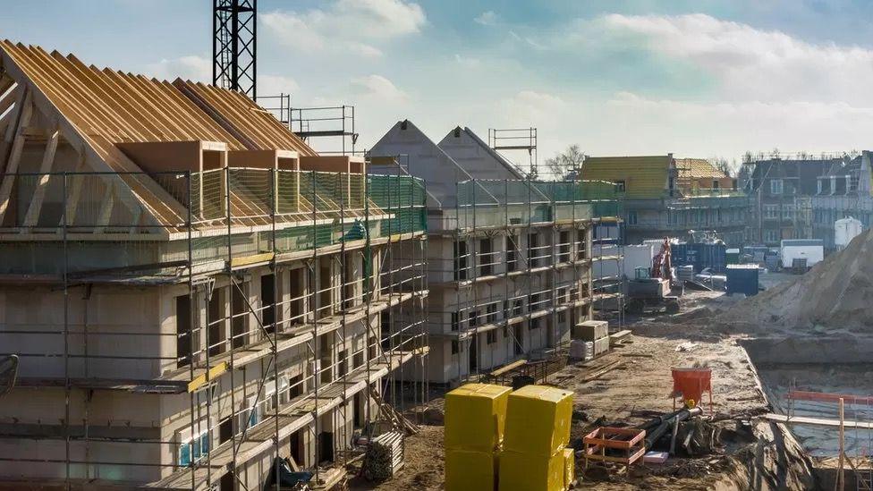 Houses being built on land with construction equipment stacked high.