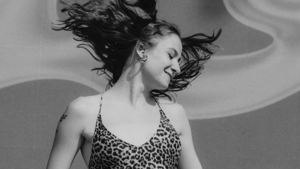 A woman is dancing. Her hair is flying up in the air. She is wearing a leopard print top.