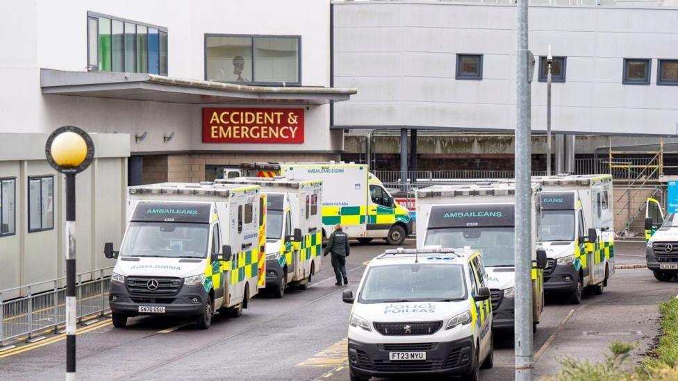 The entrance to the Victoria hospital - there are various ambulances parked outside and a sign indicating the entrance to the A & E department 