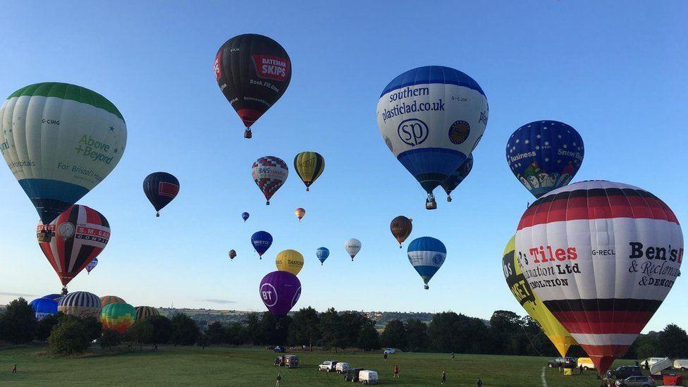 Around 20 colourful hot-air balloons rising into a blue sky at dawn