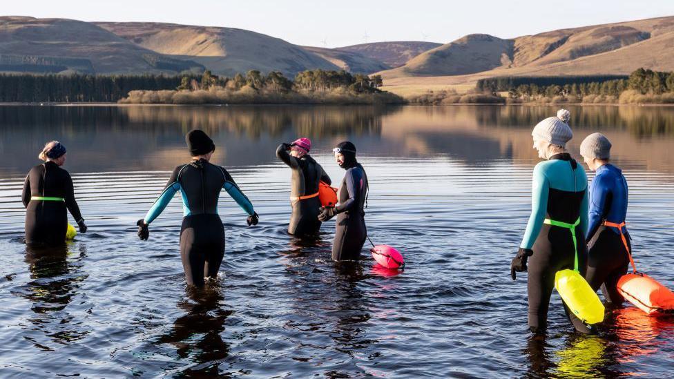 Swimmers in wetsuits entering the water