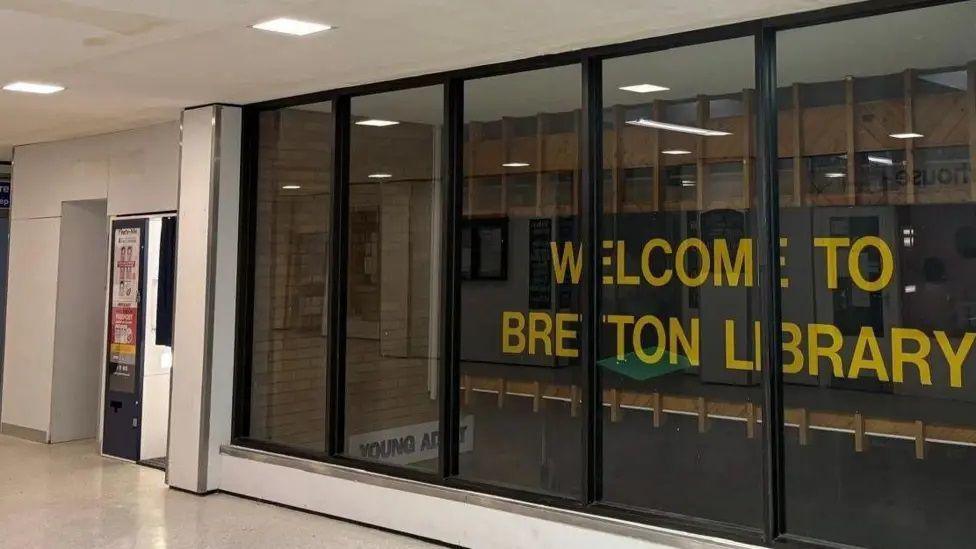 Sign reads 'Welcome to Bretton Library' in yellow text between glass window 